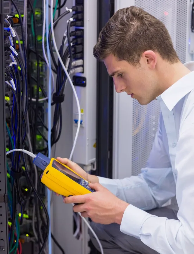 Technician testing network cabling with a handheld analyzer in a server room